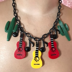 Könnte beinhalten: Eine schwarze Kettenkette mit mehreren Anhängern, darunter rote und gelbe Gitarren, grüne Kakteen und schwarze Noten.
