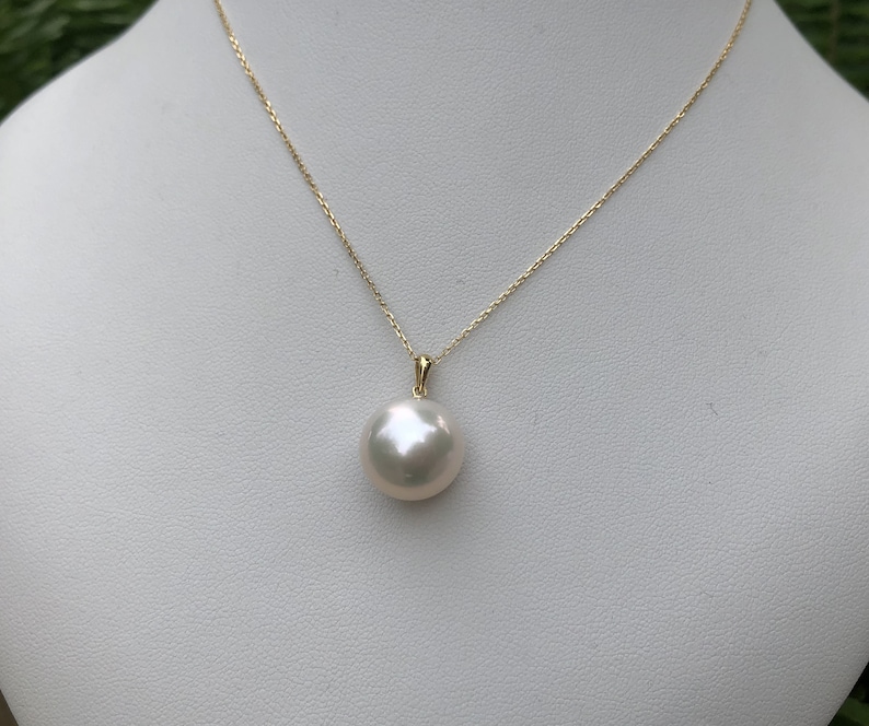 May include: A white pearl pendant necklace with a gold chain. The pearl is round and smooth.