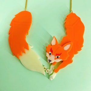 May include: Orange and white fox necklace with a gold chain. The fox is depicted with a fluffy tail and a playful expression.