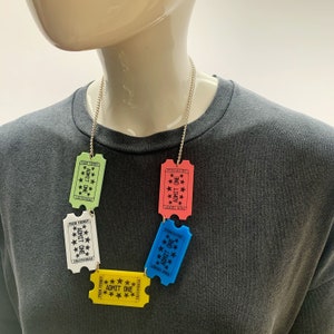 May include: A silver chain necklace with five colorful plastic ticket charms. The tickets are green, white, blue, pink, and yellow. Each ticket says "Fair Ticket" and "Admit One".