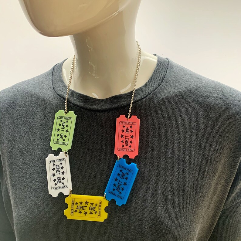 May include: A silver chain necklace with five colorful plastic ticket charms. The tickets are green, white, blue, pink, and yellow. Each ticket says "Fair Ticket" and "Admit One".