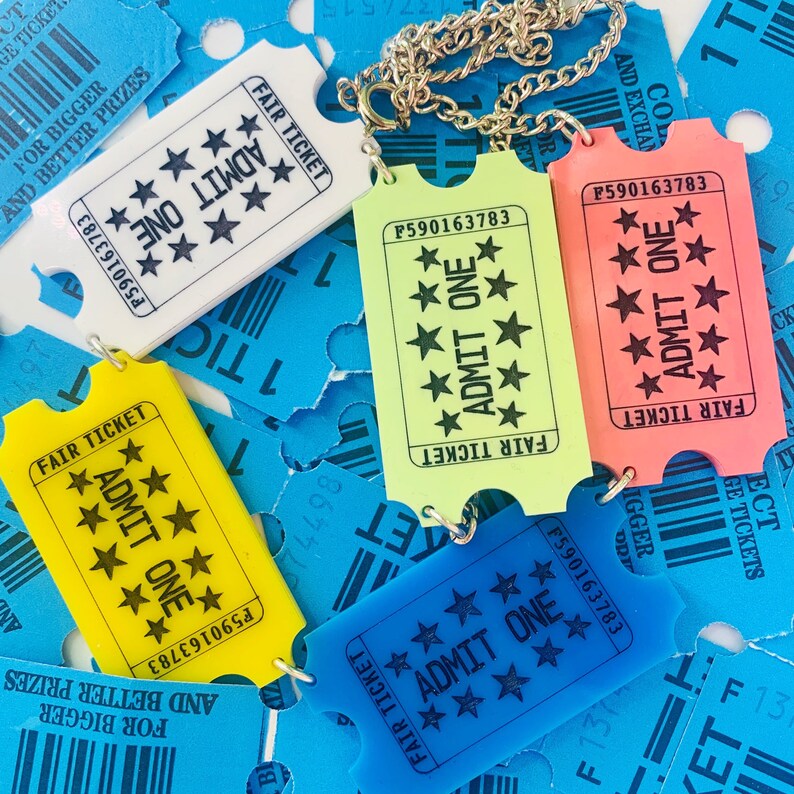 May include: A close-up of a necklace made of gold chain with five colorful plastic ticket charms. The tickets are yellow, green, blue, and pink. Each ticket has the text "Fair Ticket" and "Admit One" printed on it. The tickets have a black star pattern.