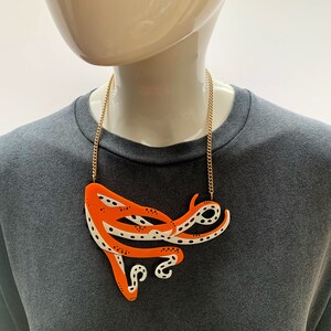 May include: A gold chain necklace with a large orange and white octopus pendant. The octopus has a spotted pattern and is in a curled position.