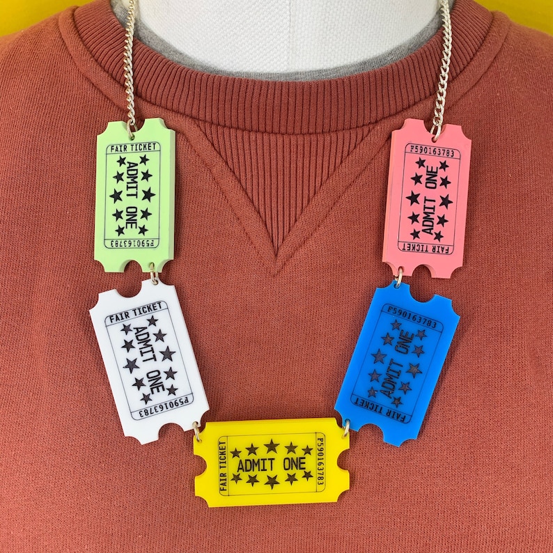 May include: A necklace made of colorful plastic ticket-shaped charms. Each charm has the text "FAIR TICKET" and "ADMIT ONE" printed on it. The charms are connected by a silver chain.