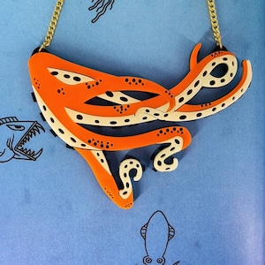 May include: Orange and white octopus necklace with a gold chain. The octopus is stylized and has a dotted pattern.
