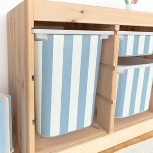 Può includere: Un armadio in legno con due contenitori di stoccaggio a strisce blu e bianche. I contenitori sono in plastica e hanno un bordo bianco.