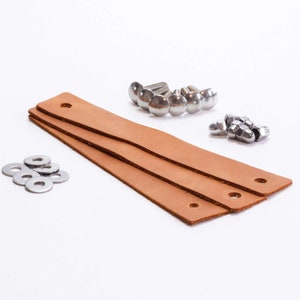 Könnte beinhalten: Drei braune Lederriemen mit Löchern zum Befestigen an einem Projekt, zusammen mit silbernen Metallschrauben, Muttern und Unterlegscheiben.