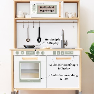 Könnte beinhalten: Weißes Spielzeug-Küchenspielset mit Mikrowelle, Backofen, Herdplatte und Spüle. Das Spielset hat einen Holzrahmen und weiße Türen mit grünen Akzenten. Das Spielset enthält eine Vielzahl von Knöpfen, Knöpfen und Displays.