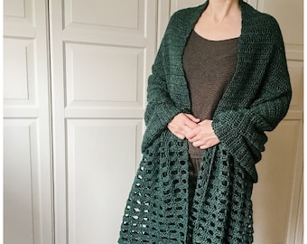 May include: A dark green crochet shawl with a lacy pattern. The shawl is draped over a person's shoulders and is tied at the front.