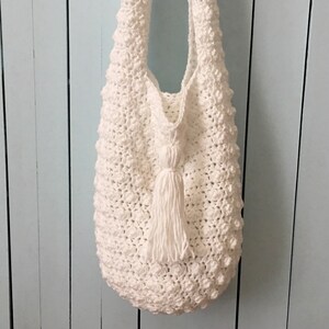 May include: White crocheted tote bag with a white tassel. The bag has a textured, bumpy surface.