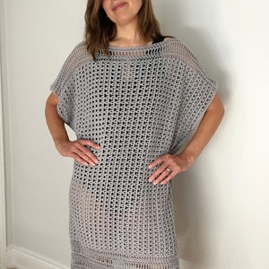 Puede incluir: Un vestido de crochet gris de corte holgado y escote amplio. El vestido tiene un patr&oacute;n simple de tejido abierto y una falda ligeramente acampanada.