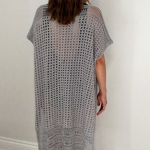 Puede incluir: Un c&aacute;rdigan de crochet gris con un dise&ntilde;o de tejido abierto y suelto. El c&aacute;rdigan tiene mangas cortas y una silueta larga y fluida.