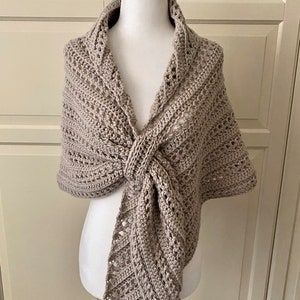 Peut inclure: Un ch&acirc;le en crochet beige avec un motif ajour&eacute; d&eacute;licat. Le ch&acirc;le est drap&eacute; sur un mannequin blanc et nou&eacute; au cou.