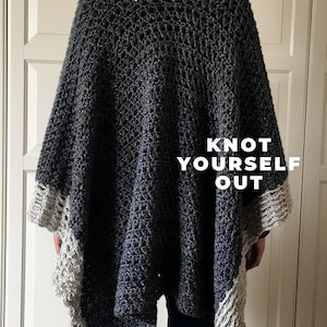 Puede incluir: Un poncho de crochet gris y blanco con un borde de flecos. El poncho tiene un tejido abierto grande y lo lleva puesto una persona. El texto "KNOT YOURSELF OUT" está impreso en la parte posterior del poncho.