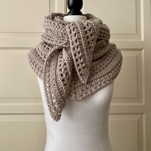 Peut inclure: Une &eacute;charpe en crochet beige avec un motif ajour&eacute;. L'&eacute;charpe est drap&eacute; autour d'un mannequin blanc.