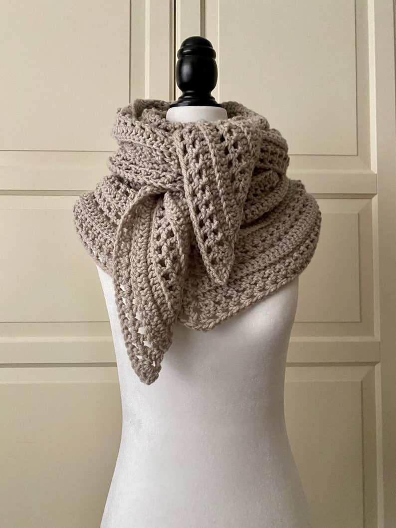 Peut inclure: Une &eacute;charpe en crochet beige avec un motif ajour&eacute;. L'&eacute;charpe est drap&eacute; autour d'un mannequin blanc.