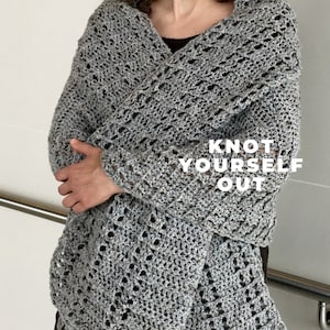 Può includere: Uno scialle all'uncinetto grigio a trama aperta con il testo "KNOT YOURSELF OUT". Lo scialle è drappeggiato sulle spalle e sulle braccia. Il motivo all'uncinetto ha un aspetto delicato e merlettato e il filato ha una sottile trama maculata.