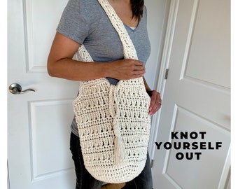 May include: A white crocheted tote bag with a long strap and a tassel. The bag is being held by a person wearing a gray shirt and jeans. The text "Knot Yourself Out" is visible in the image.