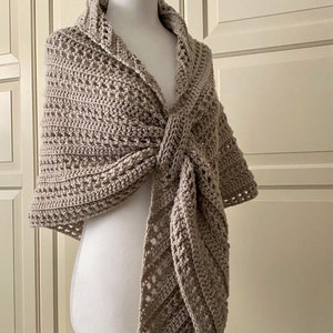 Peut inclure: Un ch&acirc;le en crochet beige avec un motif ajour&eacute; d&eacute;licat. Le ch&acirc;le est drap&eacute; sur un mannequin blanc et nou&eacute; au cou.