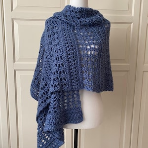 May include: A blue crocheted shawl with a cowl neck and openwork design. The shawl is displayed on a mannequin, showcasing its draped style and intricate stitch pattern. The colour is a medium shade of blue.