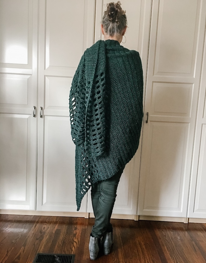 May include: A dark green crochet shawl with a lacy pattern. The shawl is draped over a person's shoulders and is worn with dark pants.