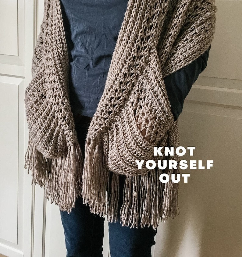 May include: A brown crocheted shawl with fringe, featuring two large pockets. The shawl is worn by a person and the text "Knot Yourself Out" is visible in the image.