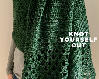 May include: A green crochet shawl with a lacy pattern. The shawl is draped over a person's shoulders and the text "Knot Yourself Out" is visible in the lower right corner of the image.