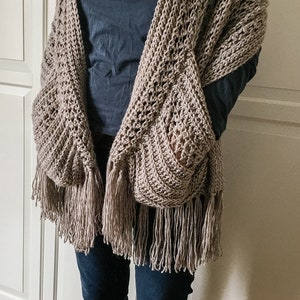 May include: A brown crocheted shawl with fringe, featuring a unique design with pockets on the sides.