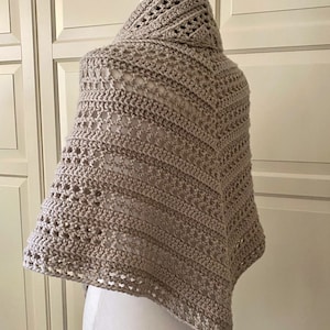 Peut inclure: Un ch&acirc;le en crochet beige avec un motif ajour&eacute; d&eacute;licat. Le ch&acirc;le est drap&eacute; sur un mannequin blanc.