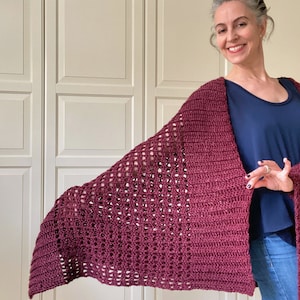 May include: A maroon crocheted shawl with a lacy pattern. The shawl is draped over the shoulders of a person wearing a blue shirt and jeans.