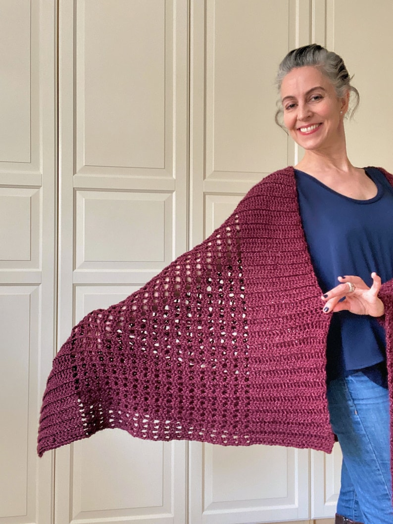 May include: A maroon crocheted shawl with a lacy pattern. The shawl is draped over the shoulders of a person wearing a blue shirt and jeans.