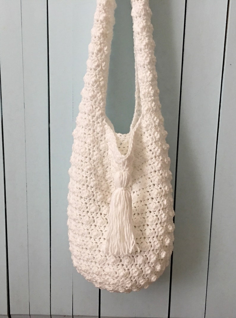 May include: White crocheted tote bag with a white tassel. The bag has a textured, bumpy surface.