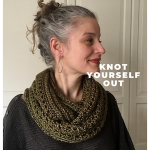 Pode incluir: Uma mulher usando uma echarpe infinita de crochê verde. O texto "KNOT YOURSELF OUT" está escrito em letras brancas sobre um fundo branco.