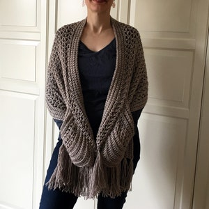 May include: A brown crocheted shawl with fringe. The shawl has a unique design with pockets on the sides.