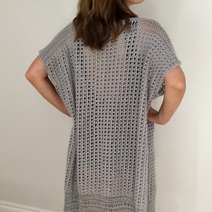 Puede incluir: Un c&aacute;rdigan de crochet gris claro con un ajuste holgado y un delicado patr&oacute;n de calado. El c&aacute;rdigan tiene mangas cortas y una silueta larga y fluida.