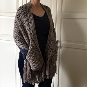 May include: A brown crocheted shawl with fringe. The shawl has a large pocket on one side.