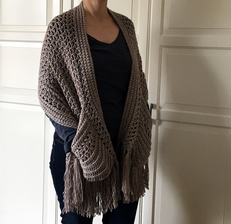 May include: A brown crocheted shawl with fringe. The shawl has a large pocket on one side.