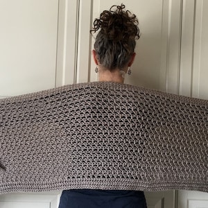 May include: A brown crocheted shawl with fringe on the edges. The shawl is draped over a person's shoulders.