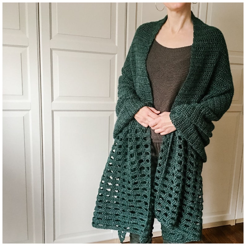 May include: A dark green crochet shawl with a lacy pattern. The shawl is draped over a person's shoulders and is worn with a brown tank top.