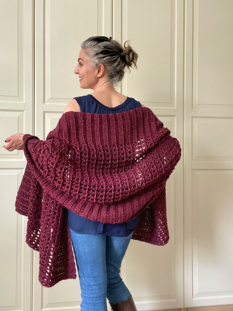 May include: A maroon crocheted shawl with a lacy pattern. The shawl is draped over the shoulders of a person wearing a navy blue tank top and blue jeans.
