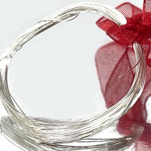 May include: A coil of shiny, silver-colored wire, possibly jewelry wire or craft wire, is the primary focus. A sheer, red ribbon is tied around the wire, adding a decorative element. The background is a bright, neutral color.