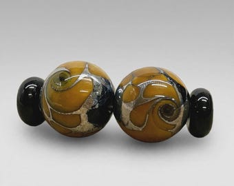 May include: Two spherical glass beads featuring a mustard yellow base with swirling silver metallic inclusions and dark black accents, flanked by two smaller, solid black glass spacer beads on either side of the main focal pieces.