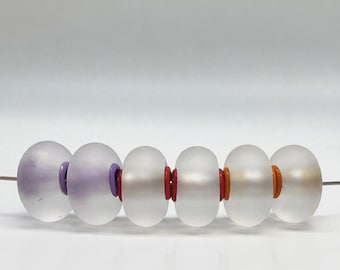 May include: A horizontal row of six frosted, translucent, round beads strung on a thin wire. The beads are separated by small, solid-colored spacer rings in purple, red, and orange, creating a colorful, repeating pattern.