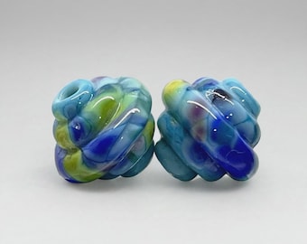May include: Two spherical glass beads featuring a swirling marbled pattern of vibrant blue, lime green, and white colors. Each bead has a smooth, glossy finish with a central hole visible on the top surface, showcasing a complex, multi-colored design.