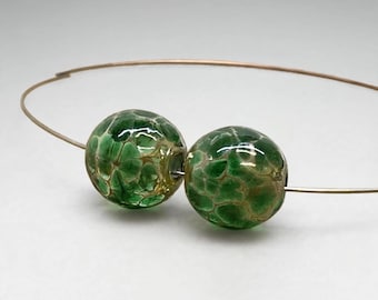 May include: A necklace featuring two spherical glass beads strung on a thin metallic wire. The beads are a deep emerald green color with a translucent, crackled texture that reveals a lighter, golden-brown webbed pattern throughout the surface.