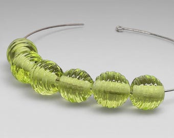 May include: A necklace featuring five translucent, lime-green glass beads with a ribbed, circular texture. The beads are strung on a thin, flexible silver-toned metal wire that forms a curved, open-ended collar shape around the neck area.