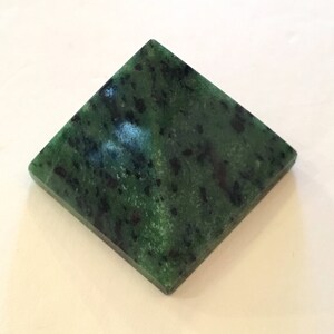 May include: A green pyramid-shaped crystal with black flecks.