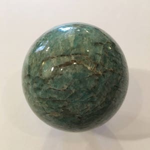 May include: A green aventurine sphere with a smooth, polished surface. The sphere has a natural, marbled pattern with light and dark green hues.