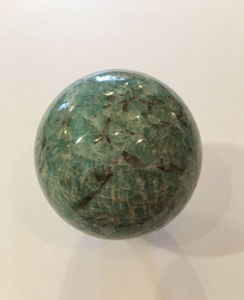 May include: A green and white sphere made of polished amazonite. The sphere has a smooth, polished surface with a natural, marbled pattern.
