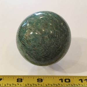 May include: A smooth, green, polished sphere of amazonite, a variety of microcline feldspar, with a diameter of approximately 2.5 inches.
